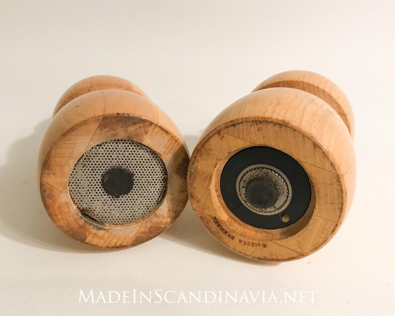 May include: Two wooden salt and pepper grinders with a light wood finish. The grinders have a rounded shape with a small knob on top and a metal mesh or grinding mechanism on the bottom. The text "MADEINSCANDINAVIA.NET" is at the bottom.