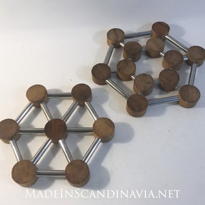 Puede incluir: Dos salvamanteles de madera con diseño geométrico. Cada salvamanteles presenta pequeñas piezas redondas de madera conectadas por varillas metálicas plateadas. Los salvamanteles están dispuestos sobre una superficie blanca.
