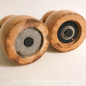 May include: Two wooden pepper grinders with a light brown finish. The bottom of each grinder features a metal mesh and a black center. The text "MADEINSCANDINAVIA.NET" is visible at the bottom.
