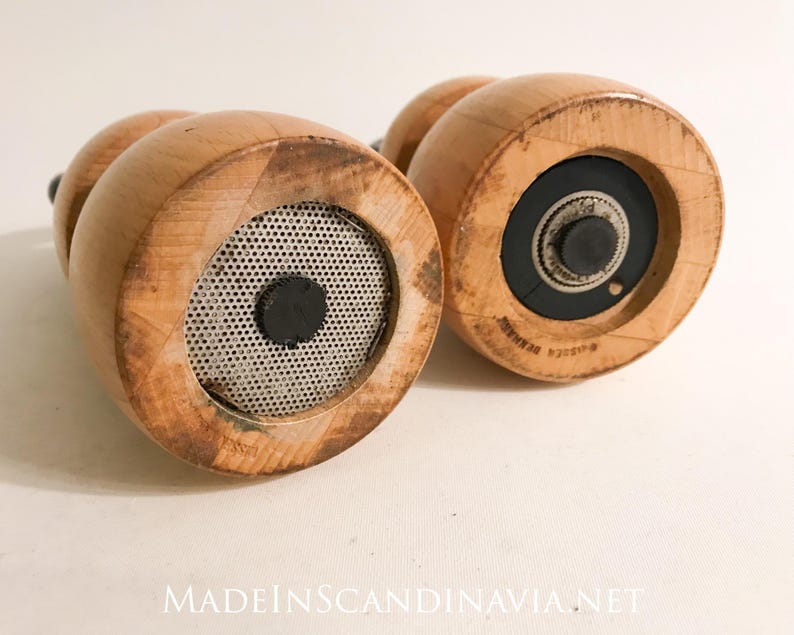 May include: Two wooden pepper grinders with a light brown finish. The bottom of each grinder features a metal mesh and a black center. The text "MADEINSCANDINAVIA.NET" is visible at the bottom.