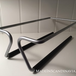 May include: A silver metal rack with two black rubber bars. The rack is designed to hold items like towels or dishcloths.