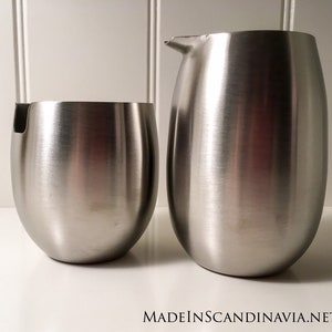 May include: Two stainless steel kitchen containers, one is a pitcher with a handle and the other is a smaller round container with a lip.