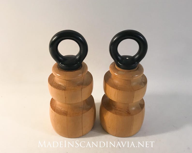 May include: Two wooden objects with a light brown finish and a black ring on top. The objects have a layered design and are set against a white background. The text "MADEINSCANDINAVIA.NET" is visible at the bottom.