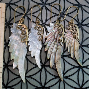 May include: A pair of gold and iridescent shell angel wing earrings. The wings are detailed with intricate filigree designs and have a natural, organic look.