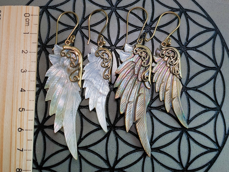 May include: A pair of gold and iridescent shell angel wing earrings. The wings are detailed with intricate filigree designs and have a natural, organic look.