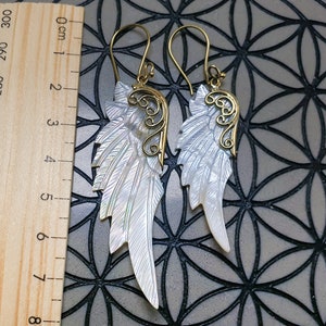May include: A pair of gold and white shell angel wing earrings. The wings are made of mother of pearl and have a delicate gold filigree design.