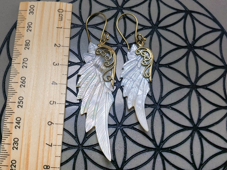 May include: A pair of gold and white shell angel wing earrings. The wings are made of mother of pearl and have a delicate gold filigree design.