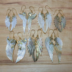 May include: A set of ten gold and white angel wing earrings. The wings are made of mother of pearl and have intricate gold details. The earrings are perfect for adding a touch of elegance to any outfit.