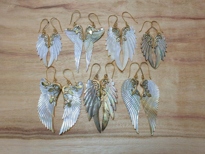 May include: A set of ten gold and white angel wing earrings. The wings are made of mother of pearl and have intricate gold details. The earrings are perfect for adding a touch of elegance to any outfit.