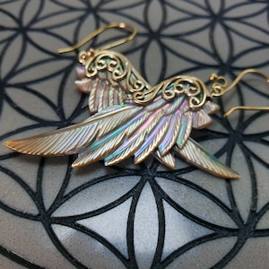 May include: A pair of iridescent abalone shell earrings with gold filigree accents and a wing shape. The earrings are hanging from gold hooks.