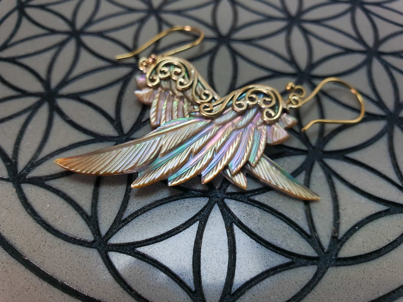 May include: A pair of iridescent abalone shell earrings with gold filigree accents and a wing shape. The earrings are hanging from gold hooks.