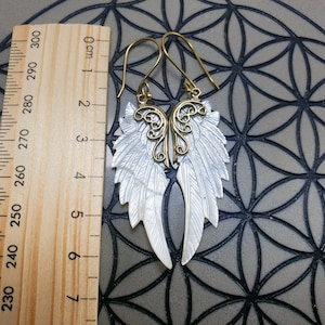 May include: A pair of gold and white angel wing earrings. The wings are made of mother of pearl and have a delicate filigree design. The earrings are approximately 6 cm long.
