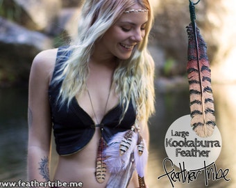 Op de afbeelding: Een grote Kookaburra-veerpendant met een zwart koord. De veer is voornamelijk bruin, rood en zwart, met een gedetailleerd patroon. De afbeelding toont ook andere veren en de tekst "Feather Tribe."