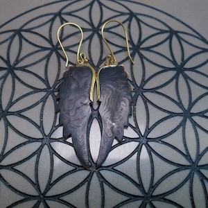 May include: A pair of dangle earrings with a gold hook and a dark brown, wood-like, leaf-shaped pendant.