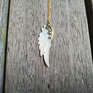 K&ouml;nnte beinhalten: Eine goldene Kettenkette mit einem wei&szlig;en Perlmutt-Engel-Fl&uuml;gel-Anh&auml;nger. Der Fl&uuml;gel hat oben ein goldenes Filigranmuster.