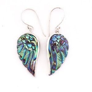 Puede incluir: Un par de pendientes de plata con alas de n&aacute;car de abul&oacute;n iridiscente. Las alas est&aacute;n talladas con un patr&oacute;n de plumas detallado y tienen una gama de colores azul, verde y morado.