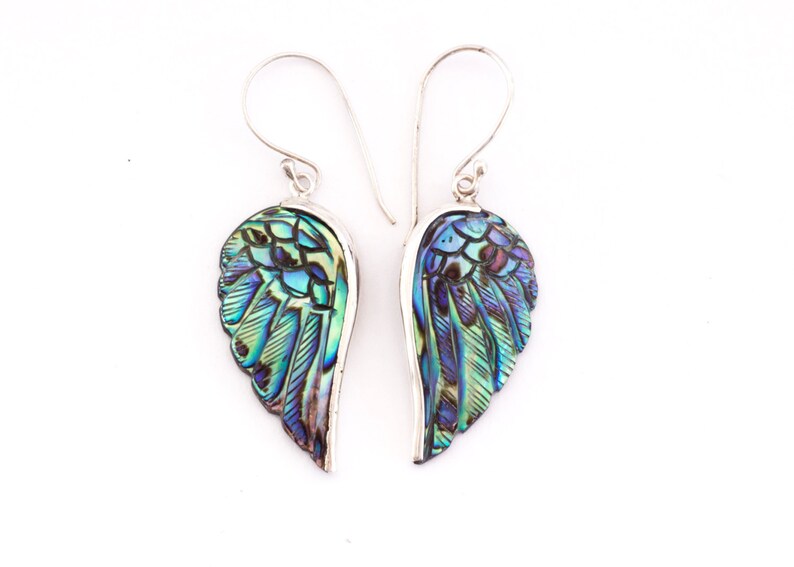Puede incluir: Un par de pendientes de plata con alas de n&aacute;car de abul&oacute;n iridiscente. Las alas est&aacute;n talladas con un patr&oacute;n de plumas detallado y tienen una gama de colores azul, verde y morado.