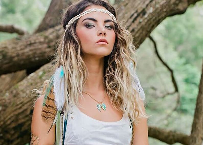 Puede incluir: Una mujer con el pelo largo y ondulado rubio que lleva una diadema blanca con un dise&ntilde;o trenzado. Lleva un top blanco sin mangas y un collar de oro con un colgante turquesa. Lleva una pluma atada al pelo.
