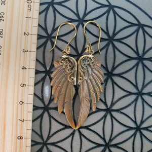 May include: Gold tone earrings with a detailed wing design. The earrings are approximately 6 cm long.