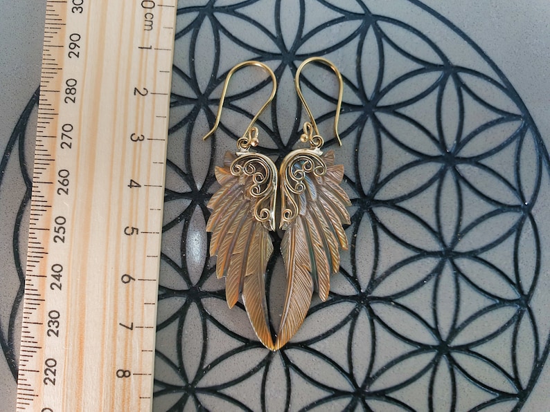 May include: Gold tone earrings with a detailed wing design. The earrings are approximately 6 cm long.