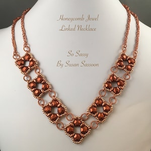 May include: A copper-toned necklace with a honeycomb design. The necklace is made of small beads and wire, and it has a V-shaped neckline. The necklace is called "Honeycomb Jewel Linked Necklace" and is by "So Sassy by Susan Sassoon".