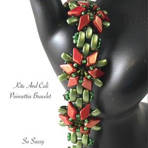 May include: A red and green beaded bracelet with a silver charm. The bracelet is made with small, faceted beads and features a poinsettia design. The text "Kite And Cali Poinsettia Bracelet" and "So Sassy By Susan Sassoon" is visible on the image.