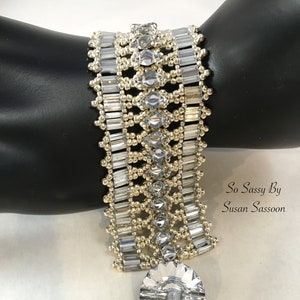 May include: A silver-toned beaded bracelet with rectangular and square-cut gems. The bracelet has a large, round, faceted gem pendant. The text "Netted Gems Bracelet" and "So Sassy By Susan Sassoon" are visible.
