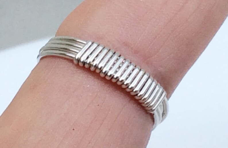May include: A silver ring made of multiple strands of wire woven together to create a textured band.