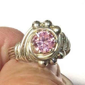 May include: A silver wire wrapped ring with a pink gemstone in the center.