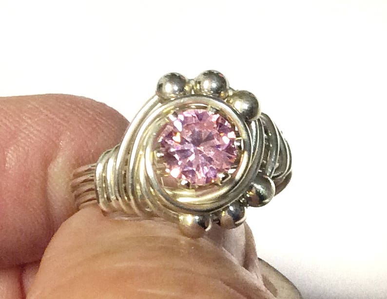 May include: A silver wire wrapped ring with a pink gemstone in the center.