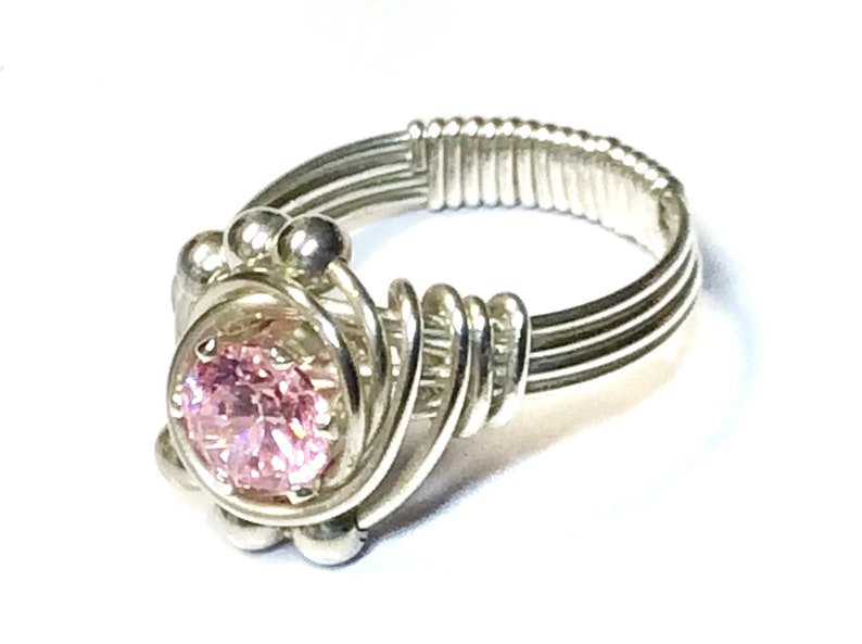 May include: A silver wire wrapped ring with a pink gemstone in the center.