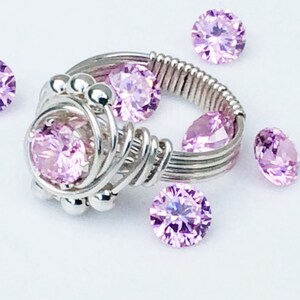 May include: A silver wire wrapped ring with a large pink gemstone in the center. The ring is surrounded by smaller pink gemstones.