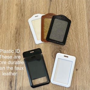 Może przedstawiać: Cztery plastikowe uchwyty na identyfikatory, dwa białe, jeden brązowy i jeden czarny. Tekst "Plastic ID These are more durable than the faux leather" jest widoczny na zdjęciu.