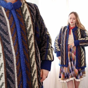 Puede incluir: Cárdigan largo estampado en tonos azules, marrones, grises y crema. El suéter presenta un diseño geométrico y una botonadura frontal. Las mangas y el cuello son de color azul liso. El cárdigan es de estilo vintage.