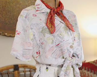Pode incluir: Um conjunto vintage de duas peças. A camisa branca com estampa colorida é amarrada na cintura, a saia branca combinando tem um design de linhas verticais pretas. Um lenço vermelho e amarelo é usado com o conjunto.