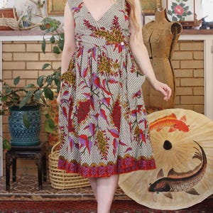 May include: A vintage-style dress with a V-neckline and a colorful floral pattern featuring red, purple, and yellow accents. The dress has a fitted bodice and a flared skirt, with a button detail at the waist. The dress is knee-length.