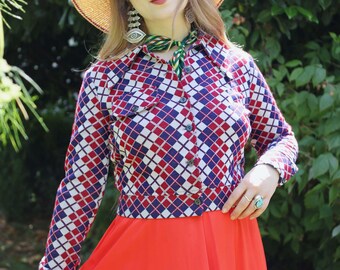 Puede incluir: Una mujer con un atuendo vintage que incluye un sombrero de paja, una camisa estampada con un diseño de rombos rojos, blancos y azules, y una falda larga de color rojo brillante. El estilo general sugiere una estética retro.
