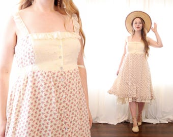 Puede incluir: Vestido de verano de estilo vintage con estampado floral y botones delanteros. El vestido presenta un corpiño color crema con detalles de ojal y tirantes con volantes. La falda es de color rosa claro con pequeños estampados florales. También se ve un sombrero de paja.