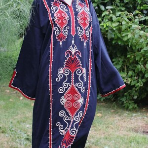 May include: A navy blue caftan with intricate red and white embroidered patterns. The long-sleeved garment features a V-neck and decorative trim along the edges. The embroidery includes floral and geometric designs.