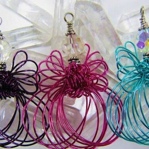 Könnte beinhalten: Drei drahtgewickelte Engels-Anhänger mit Kristallperlen. Die Engel sind aus lila, rosa und türkisfarbenem Draht gefertigt.