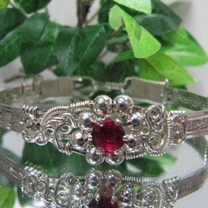 Peut inclure: Un bracelet en fil d'argent enroulé avec une grande pierre précieuse rouge au centre. Le bracelet est finement conçu avec un motif floral.