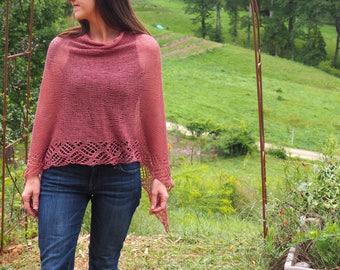 Può includere: Una donna indossa uno scialle rosa lavorato a uncinetto con un bordo di pizzo. È in piedi in un campo erboso con un arco di legno sullo sfondo.