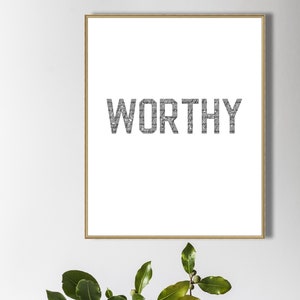 K&ouml;nnte beinhalten: Ein gerahmter Druck mit dem Wort "WORTHY" in gro&szlig;en, fetten, grauen Buchstaben. Die Buchstaben bestehen aus kleineren, &uuml;berlappenden Texten. Der Druck liegt auf einem Stapel von drei B&uuml;chern.