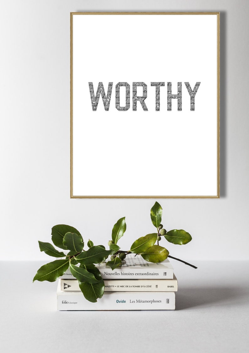 K&ouml;nnte beinhalten: Ein gerahmter Druck mit dem Wort "WORTHY" in gro&szlig;en, fetten, grauen Buchstaben. Die Buchstaben bestehen aus kleineren, &uuml;berlappenden Texten. Der Druck liegt auf einem Stapel von drei B&uuml;chern.