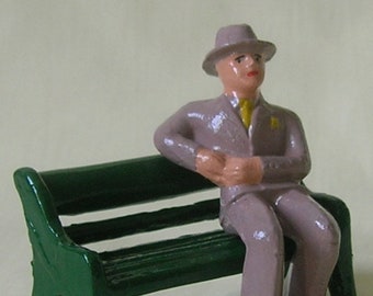 Businessman in suit sitting on park bench, collectible figurine, model train layout, hand-painted reproduction of vintage toy figure