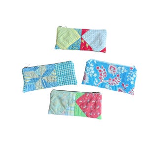 May include: Four colorful, quilted fabric zipper pouches. The pouches feature patchwork designs in various colors, including blue, green, yellow, and red. Each pouch has a zipper closure. The pouches are likely used for carrying small items.