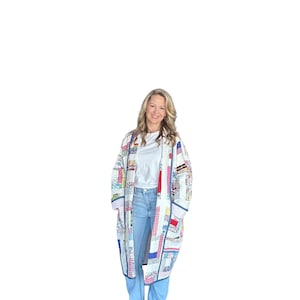 May include: A long, patchwork quilt coat in a variety of colors, including red, blue, pink, and yellow. The coat has a white background and a dark blue trim. The coat is worn over a white t-shirt and blue jeans.