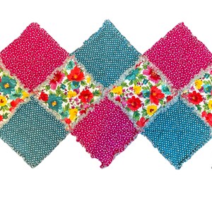 May include: A handmade, rag quilt featuring a diamond pattern. The quilt showcases alternating squares of pink polka dots, teal polka dots, and floral fabric with red, yellow, and teal flowers. The edges have a frayed, textured finish.