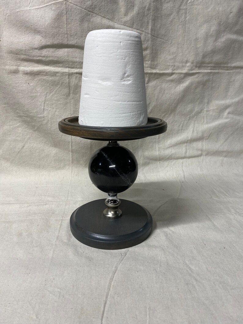 May include: A white ceramic planter sits on a black and brown wooden stand with a black marble sphere base.
