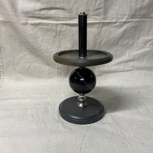 May include: A black and silver decorative stand with a round wooden top and a black marble sphere. The stand has a black metal rod extending from the top.